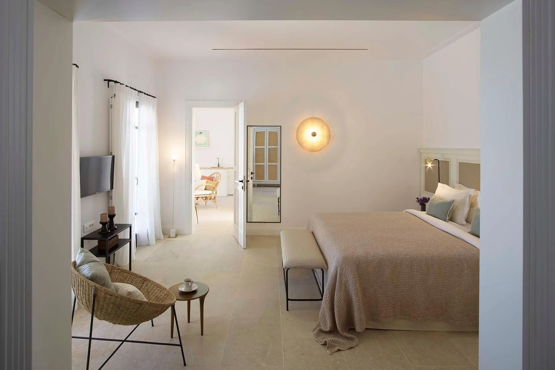 Un dormitorio luminoso con una cama tendida, una lámpara de pared y una zona para sentarse.