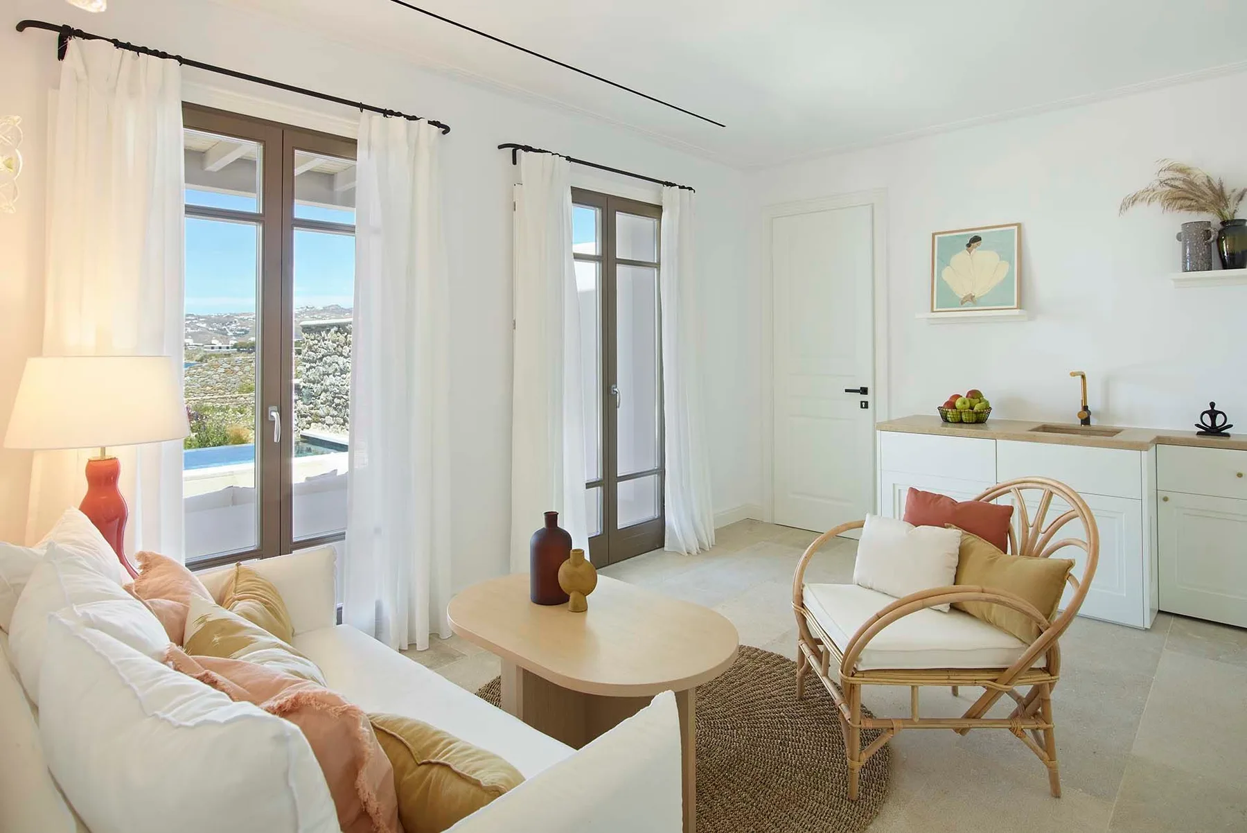 Una sala luminosa con un sofá y una silla tejida junto a ventanas altas.