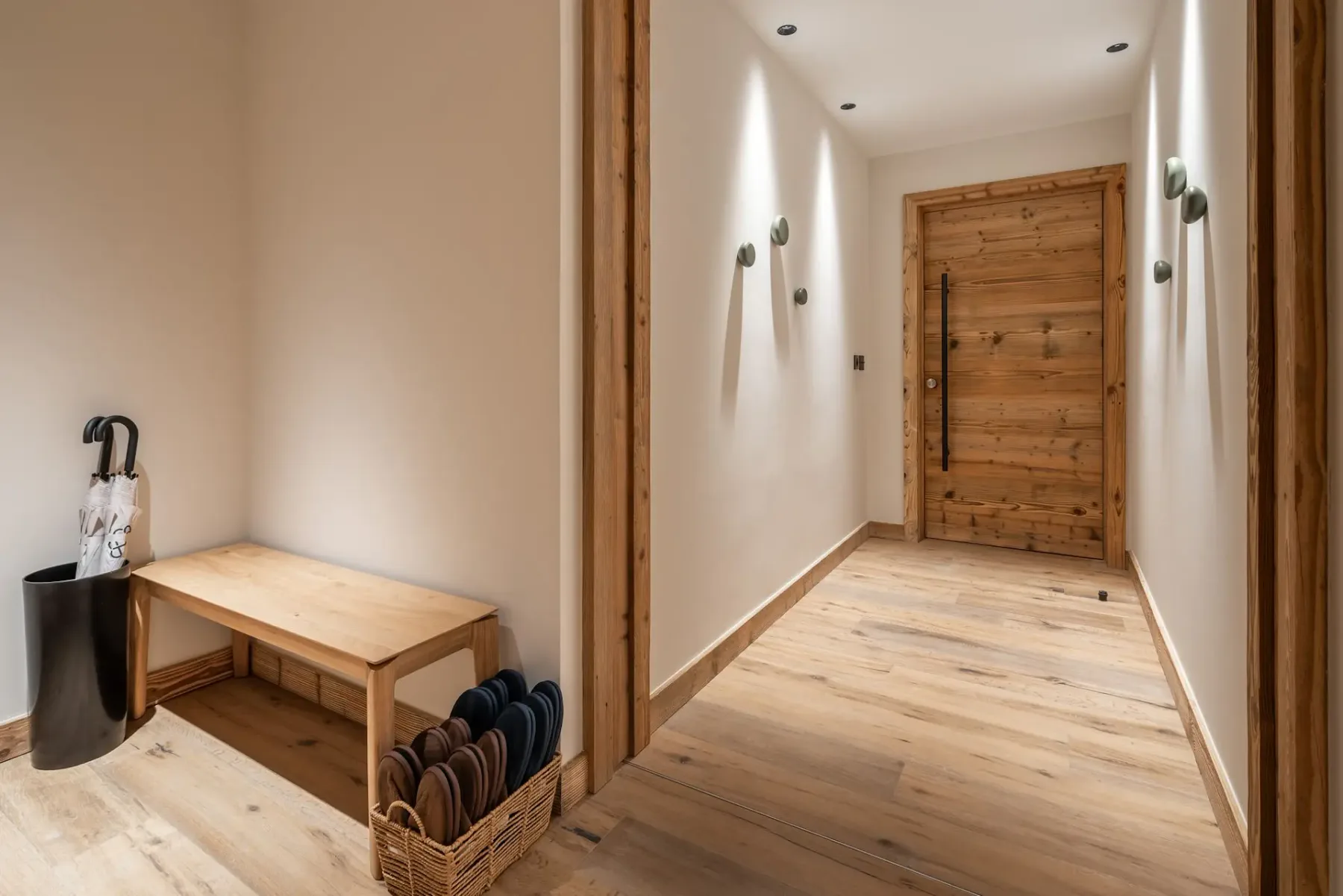 Un estrecho recibidor conduce a una puerta de madera, con un banco pequeño y una cesta para zapatos.