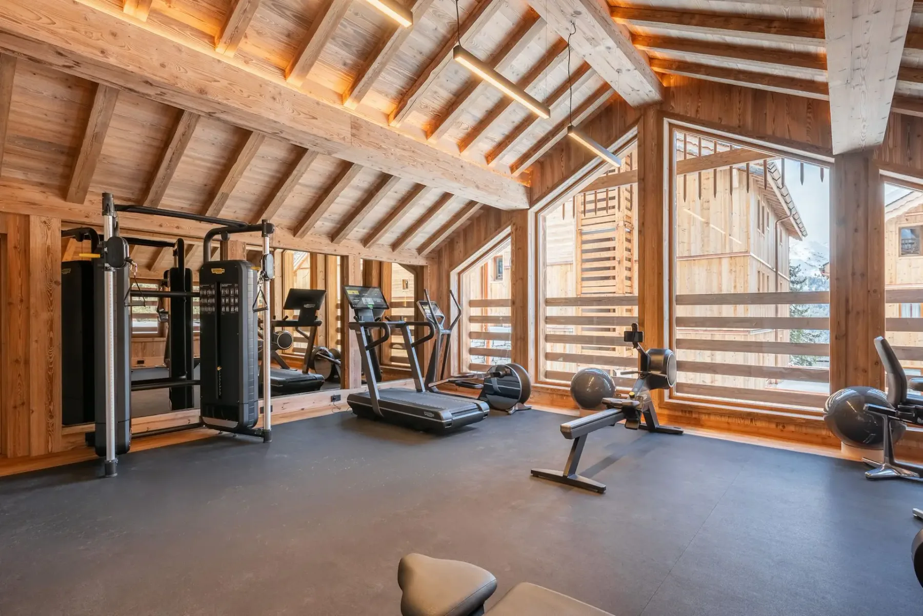 Zona común: Un gimnasio con máquinas de ejercicio y equipos cardiovasculares bajo un techo de madera.