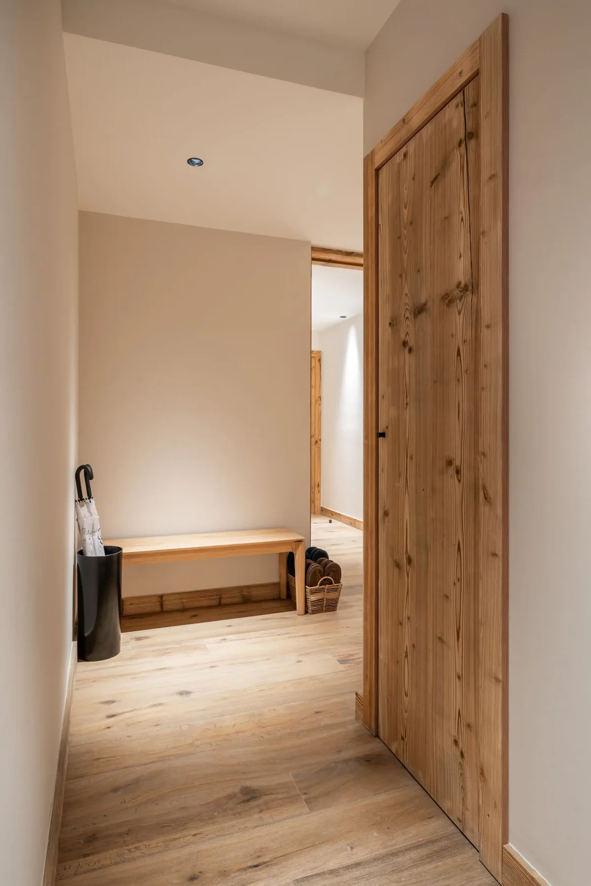 Una entrada con suelo claro, un banco de madera y una puerta de madera abierta.