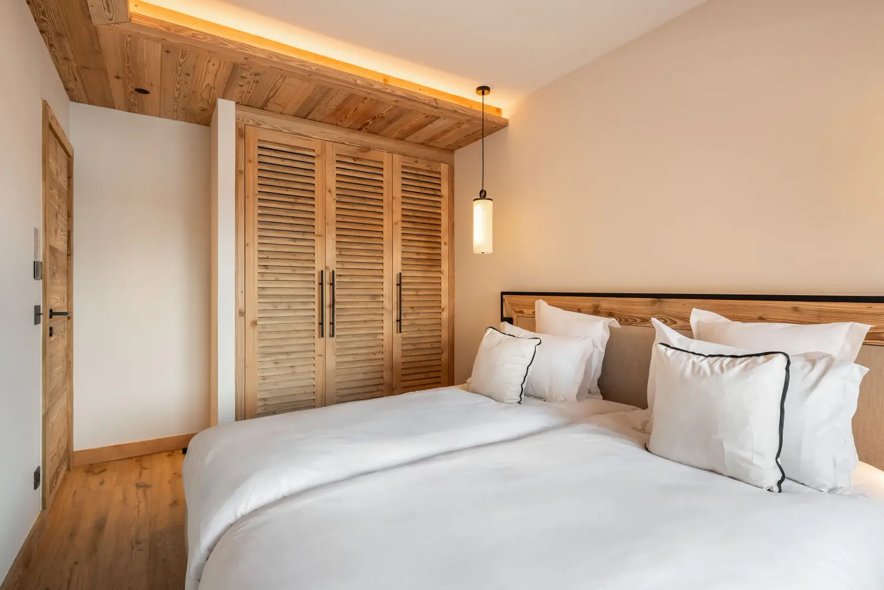 Un dormitorio con ropa de cama blanca y puertas de armario de madera con persianas.