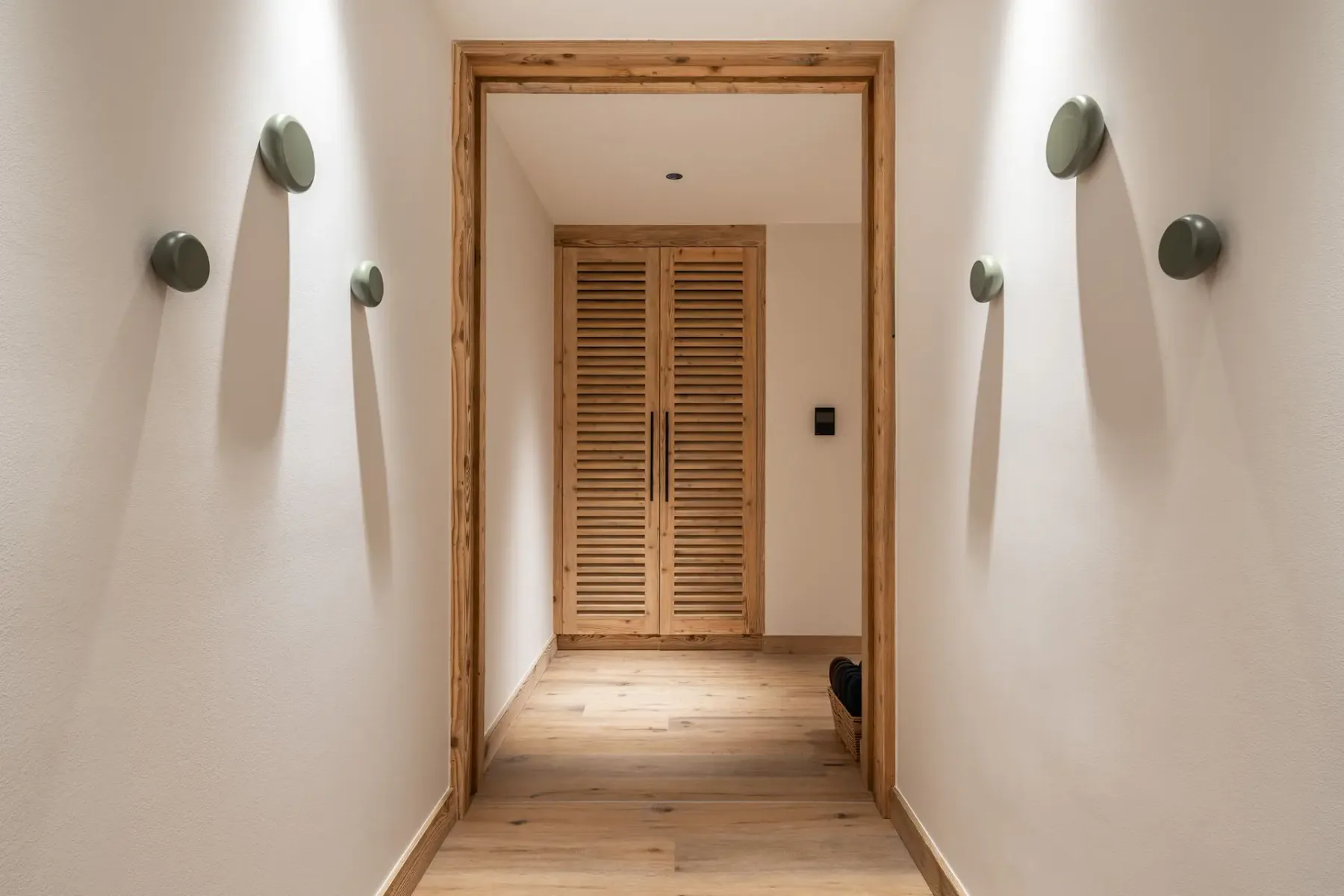 Un pasillo conduce a puertas de madera con celosías al fondo.