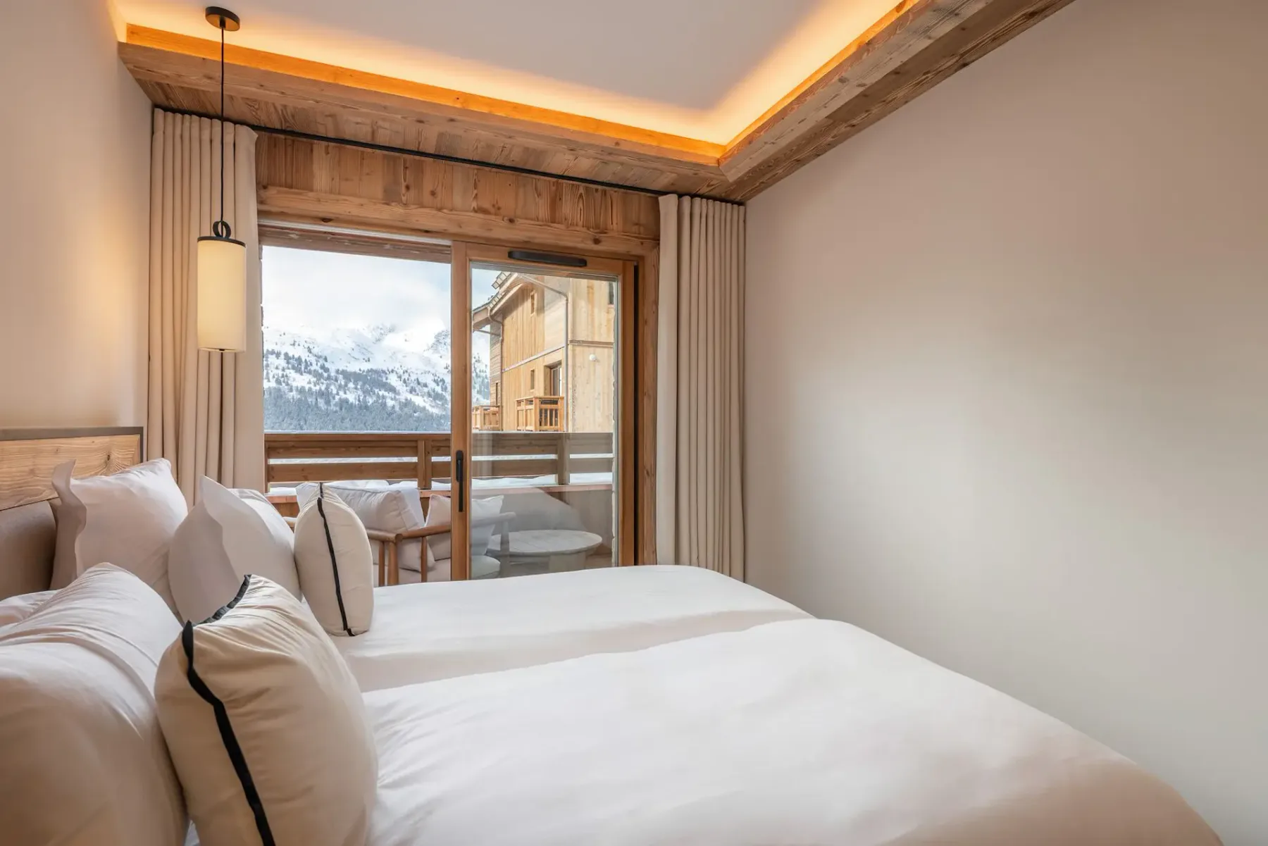 Un dormitorio con ropa de cama blanca y una ventana amplia con vistas a montañas nevadas.
