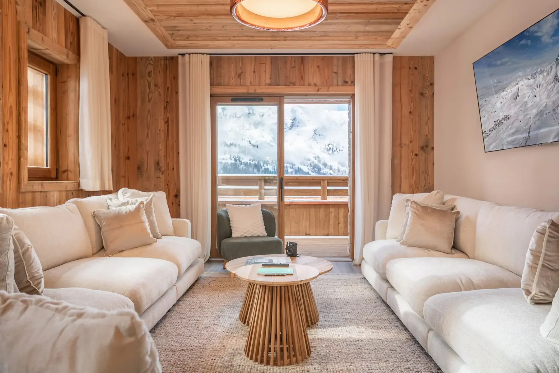 Una luminosa sala de estar con asientos claros y un balcón de madera visible tras puertas de vidrio.