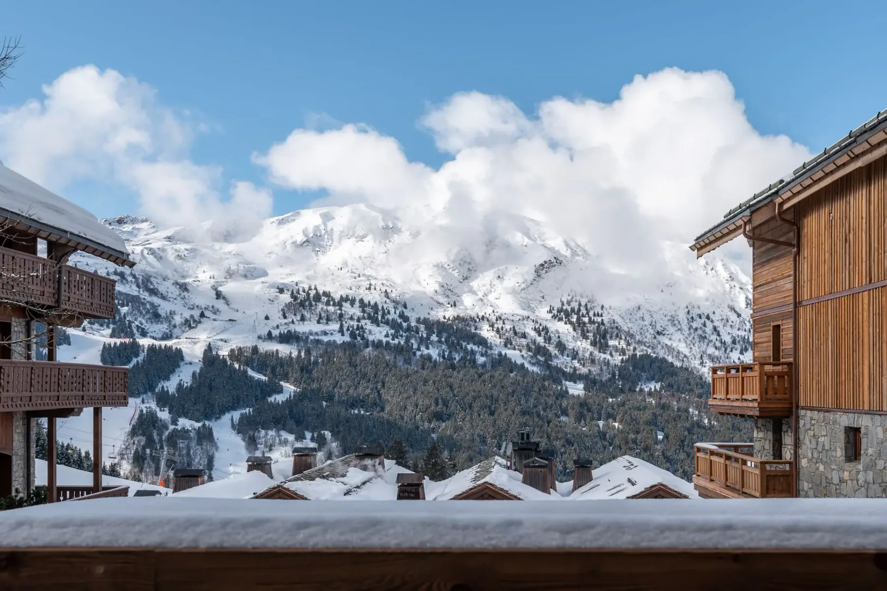 Picos nevados se elevan sobre edificios tipo chalet y un balcón de madera.