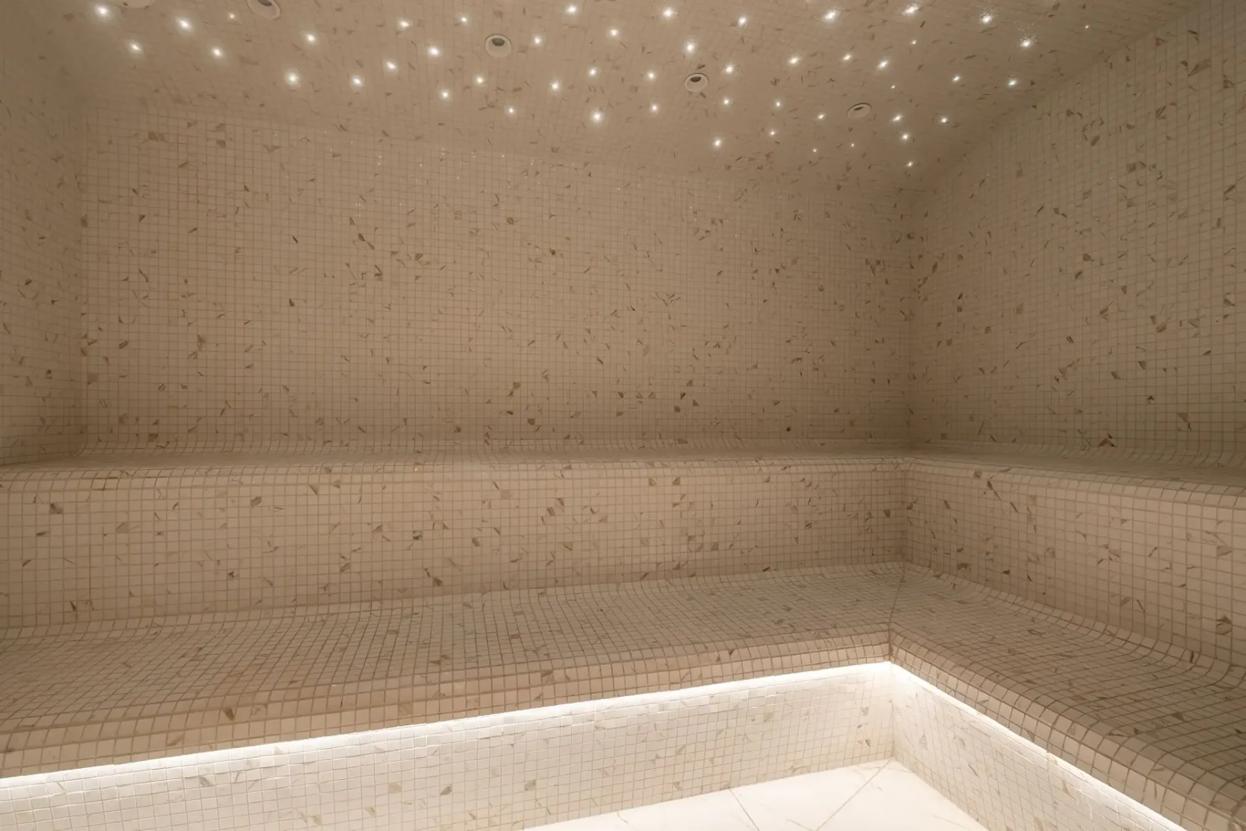 Zona común: Un baño de vapor revestido de azulejos, con un banco integrado y pequeñas luces en el techo.