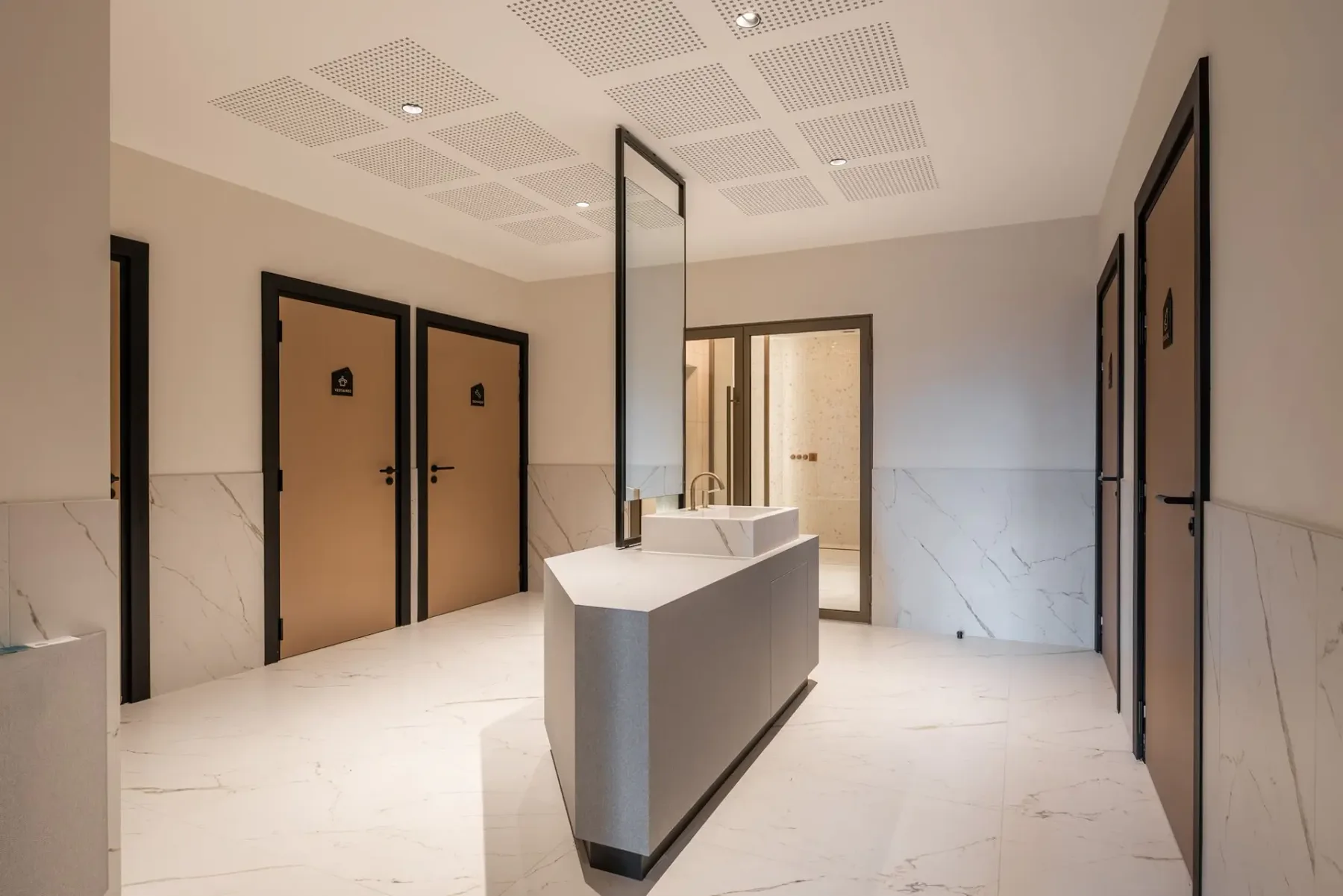 Zona común: Un área de baños luminosa con un lavabo central y varias puertas.