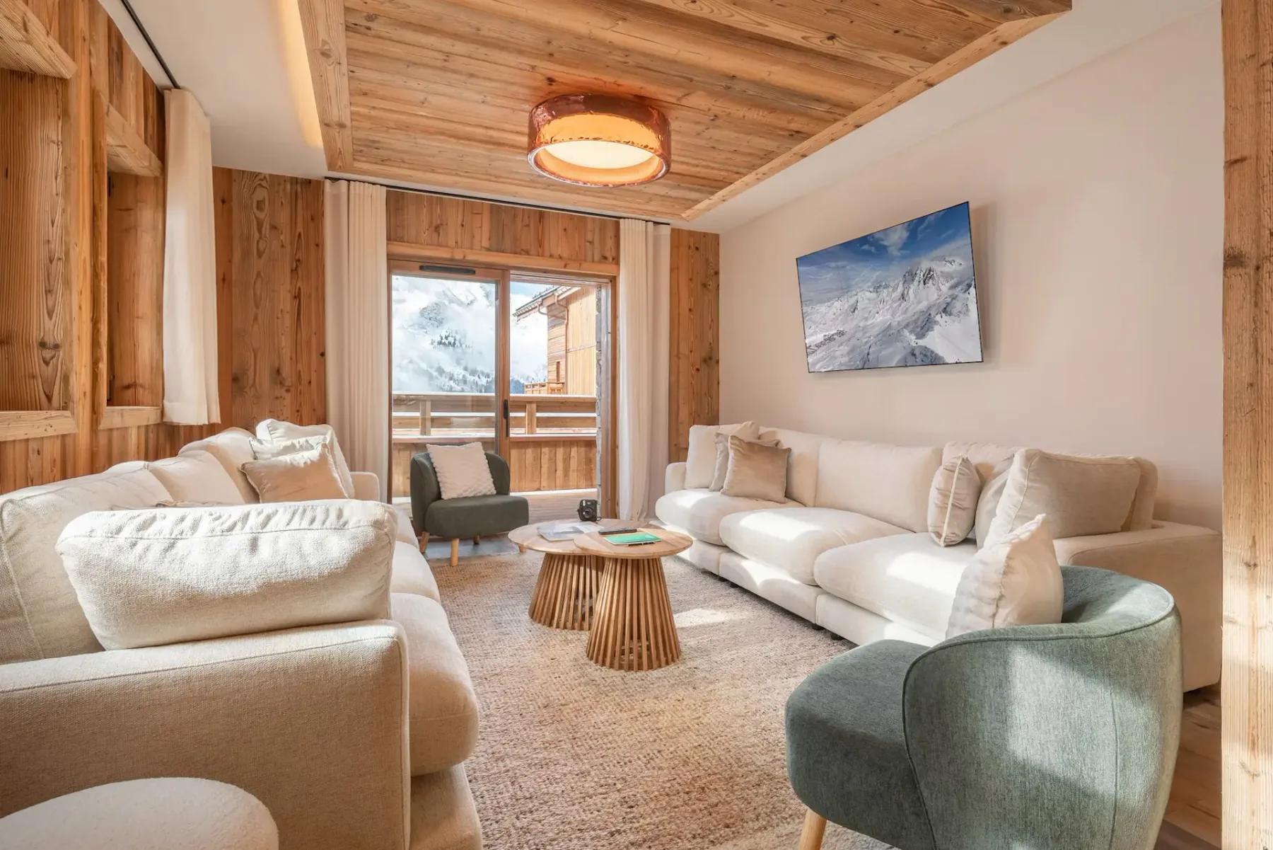 Una sala de estar con asientos claros, una mesa de centro redonda de madera y vistas a montañas nevadas.