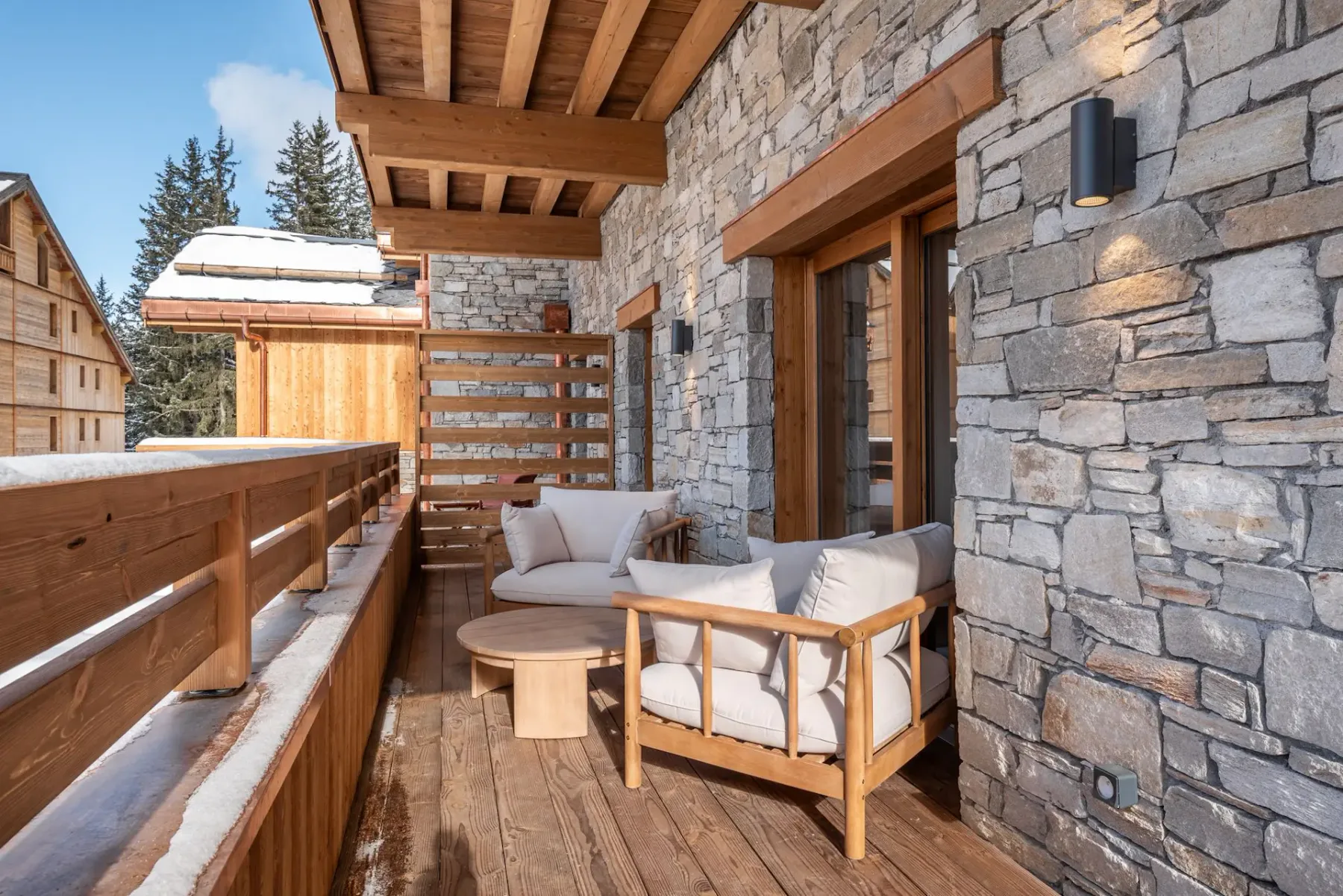 Un balcón de madera cubierto con asientos acolchados junto a una pared exterior de piedra.