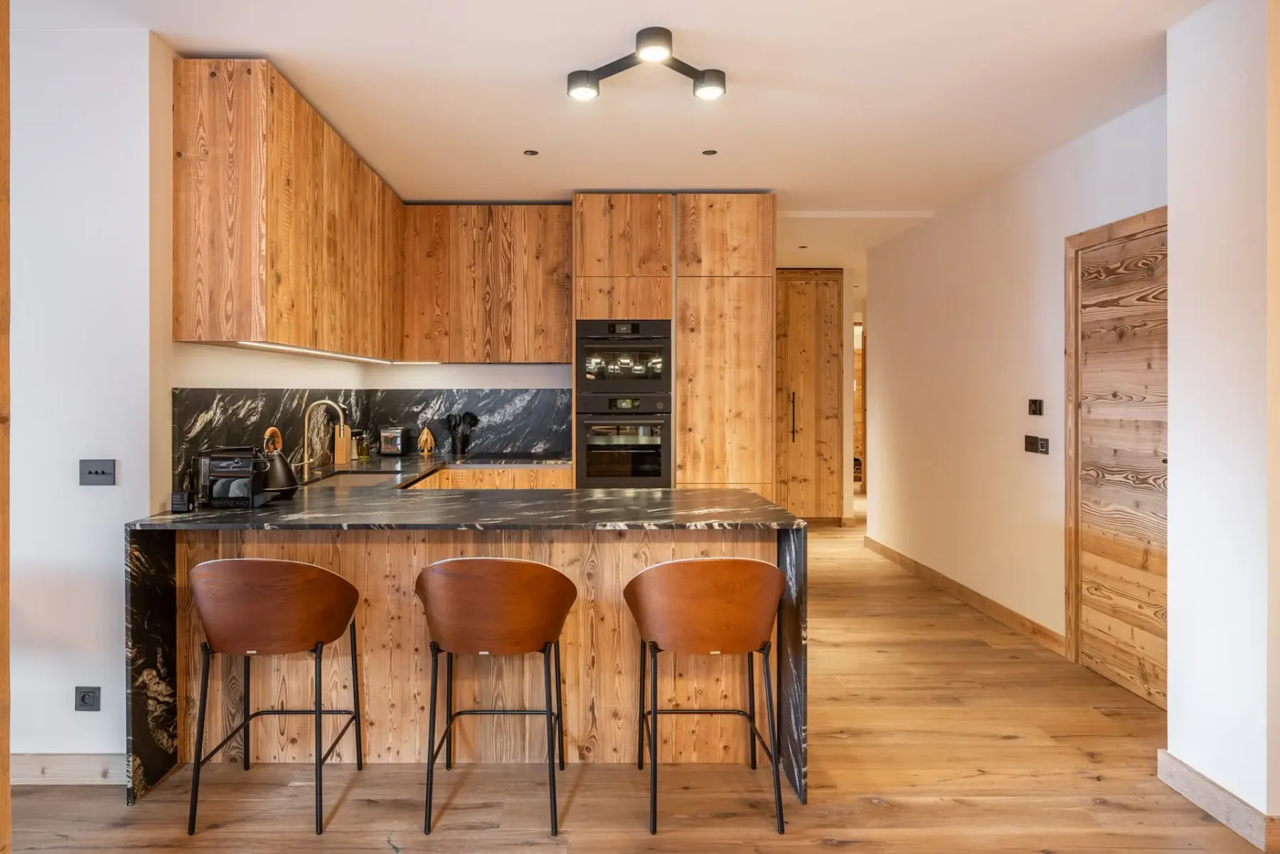 Una cocina con acabados de madera, una barra y tres taburetes.
