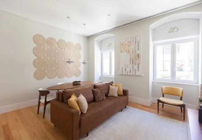A bright living room with brown seating, a light rug, and tall windows.