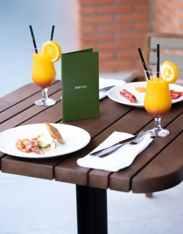 Espacio representativo del hotel: Una mesa de cafetería está preparada con bebidas, platos de comida y cubiertos.