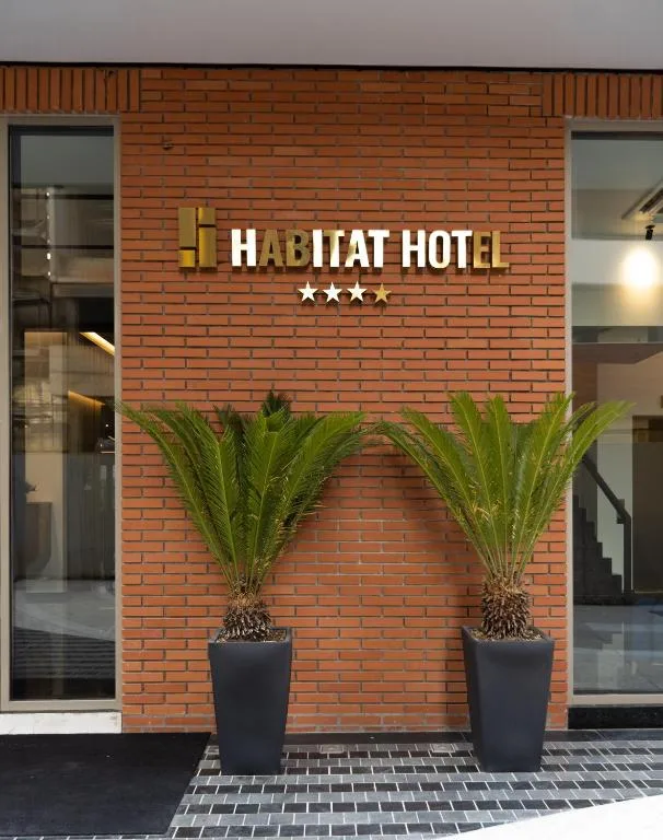 Espacio representativo del hotel: Entrada del hotel con una pared de ladrillo, un letrero y plantas en macetas.