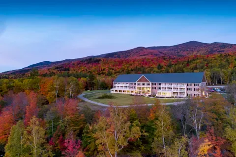 Espacio representativo del hotel: Un gran edificio hotelero se encuentra entre árboles otoñales de colores, bajo una cordillera.