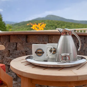 Espacio representativo del hotel: Una mesa de patio sostiene una bandeja de café junto a un muro de piedra, con vistas a la montaña.