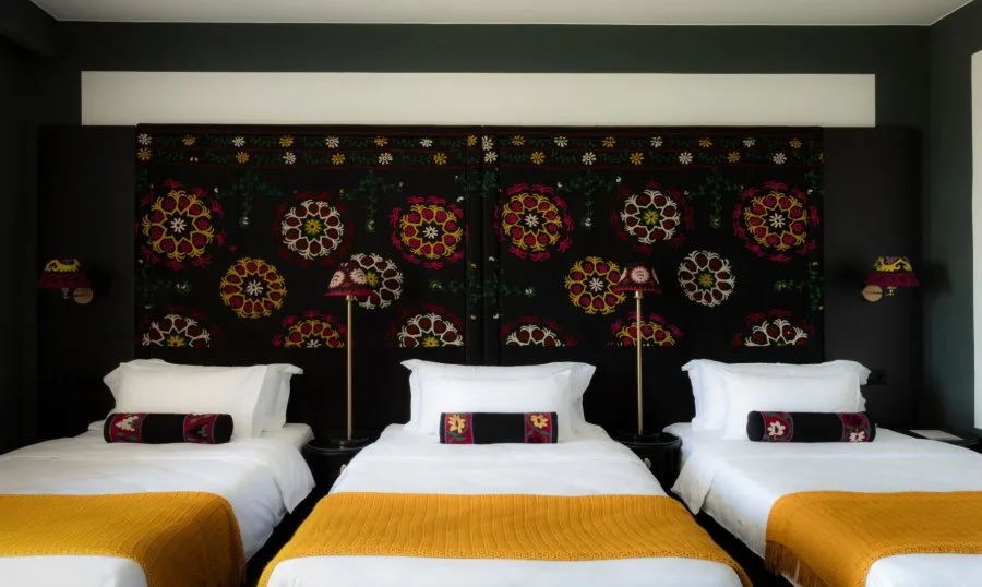 Representative hotel space: A hotel bedroom with three beds arranged beneath a colorful patterned wall hanging.