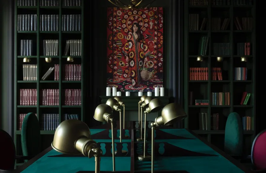 Representative hotel space: A library with tall bookshelves, a central table, and brass lamps.