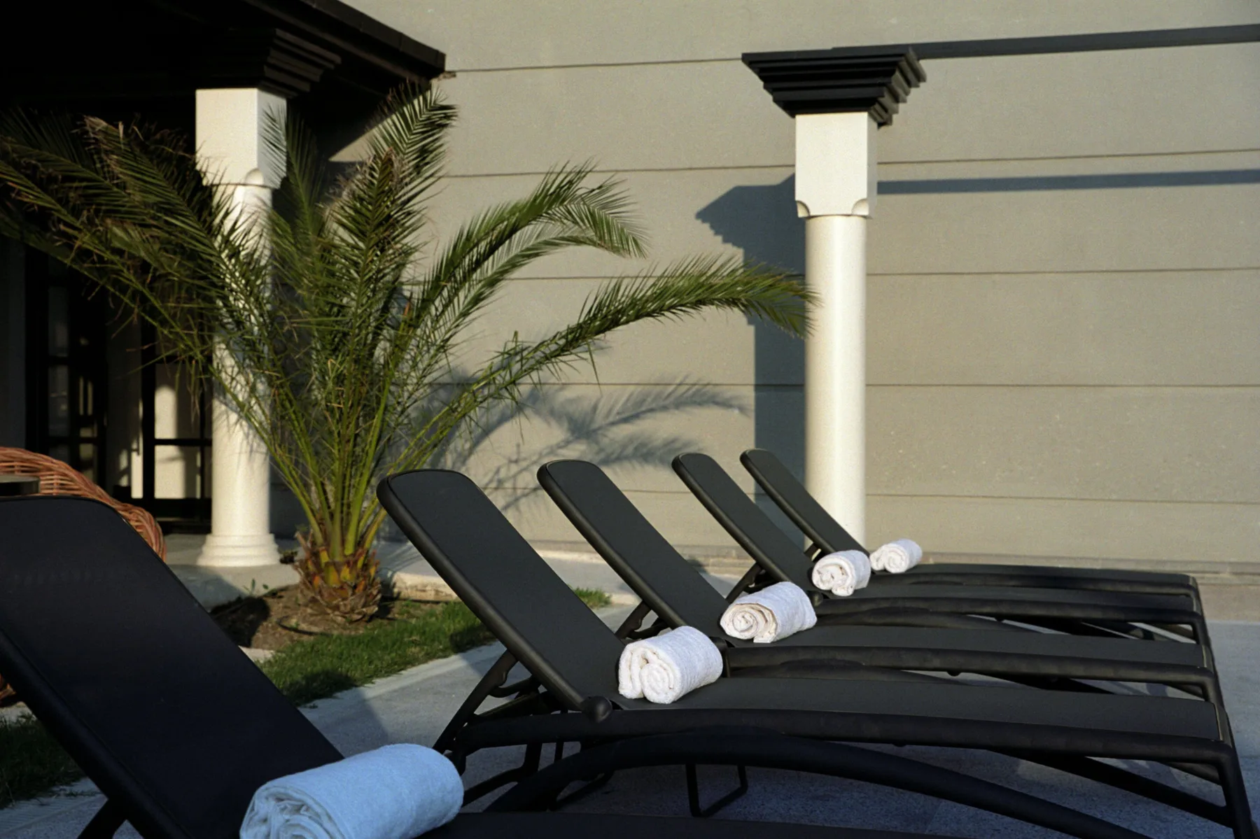 Representative hotel space: Outdoor poolside seating with towels beside a palm tree and building.