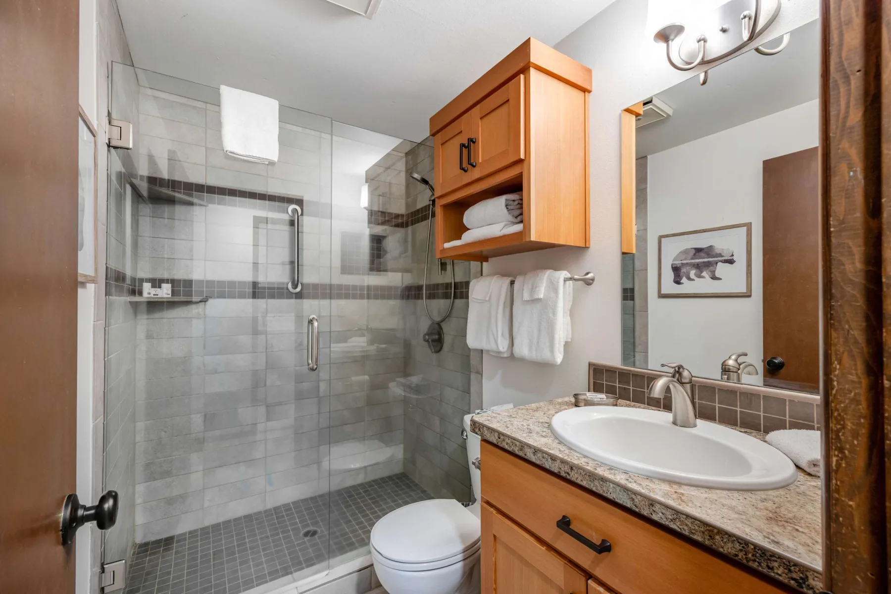 A bathroom with a glass shower, toilet, and a wood vanity with a sink.