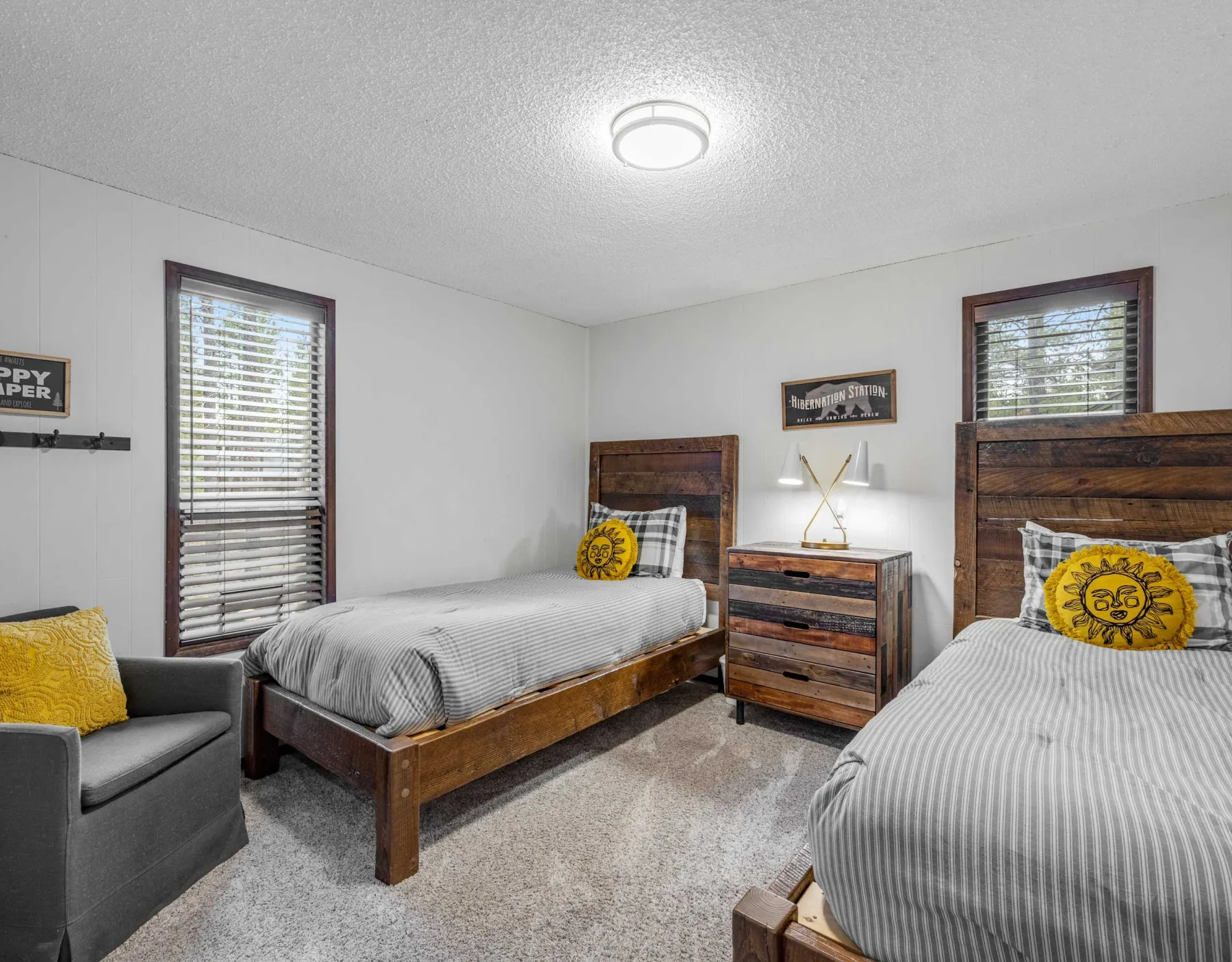 A bedroom with two beds, a dresser, and windows with blinds.