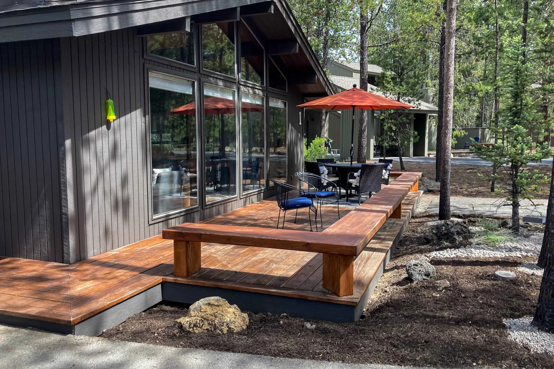 A modern cabin opens onto a wooden deck with outdoor seating and a red umbrella.