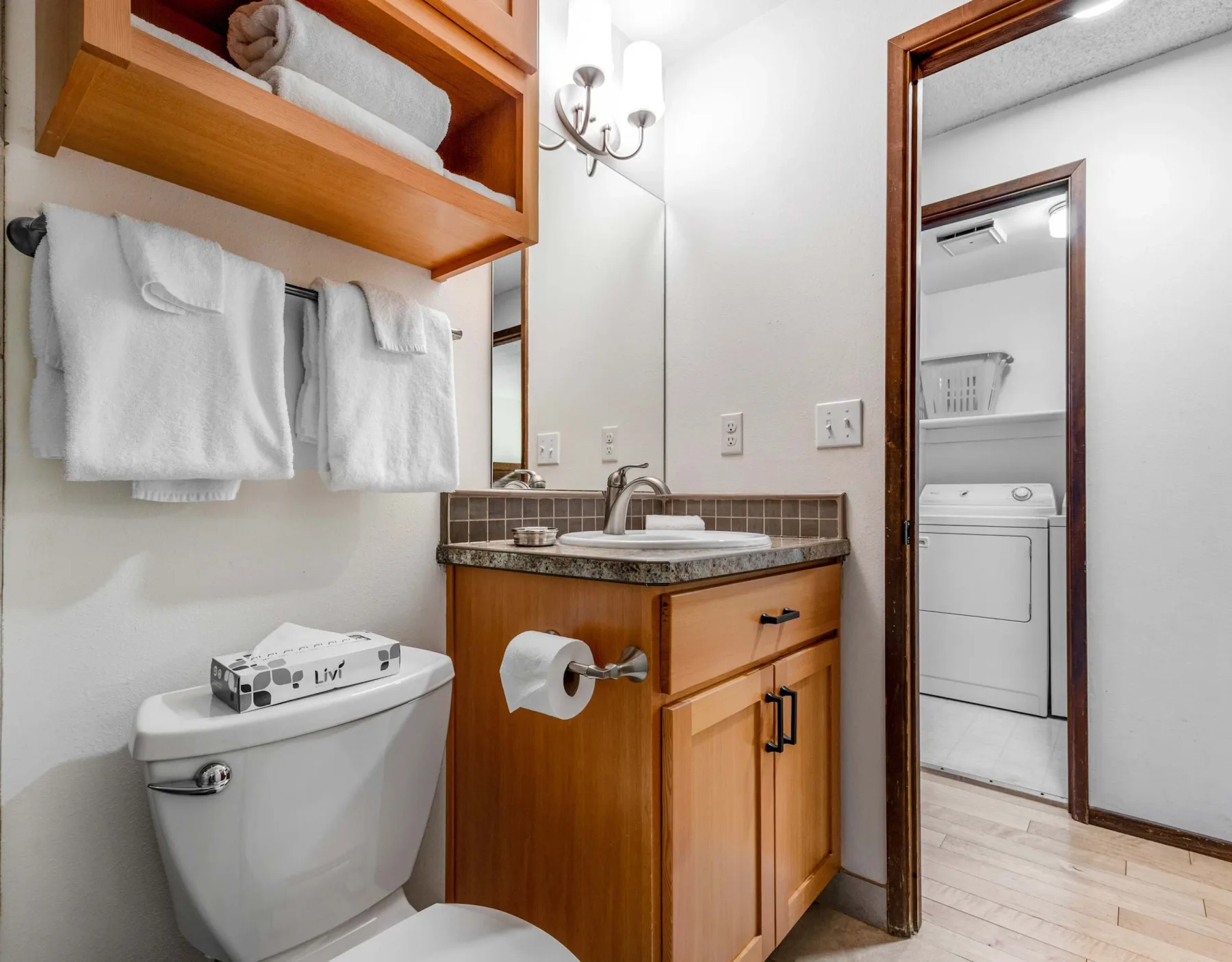 A bathroom vanity and toilet sit beside an open doorway to a laundry area.