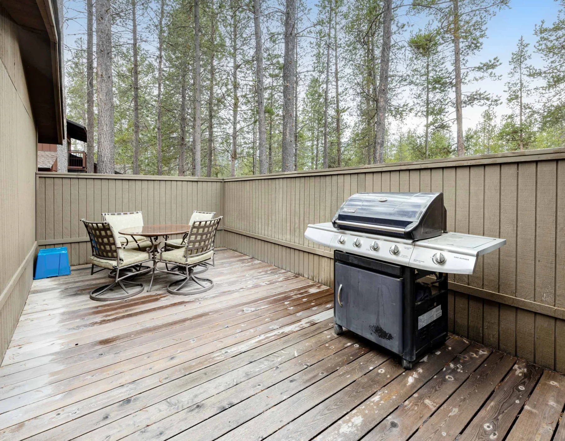 A wooden deck with outdoor seating and a barbecue grill, surrounded by trees.