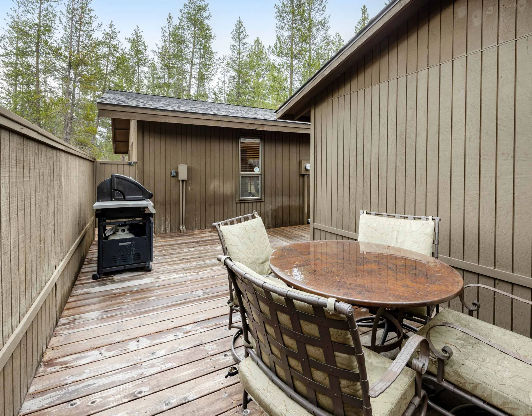 A wooden deck with an outdoor dining table, seating, and a grill.