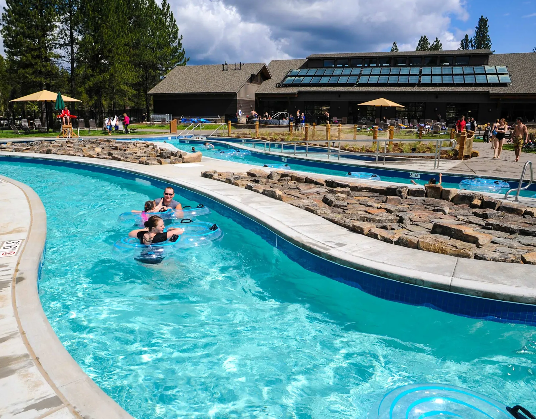 Shared amenity: Outdoor swimming pools with people in the water and a building behind them.