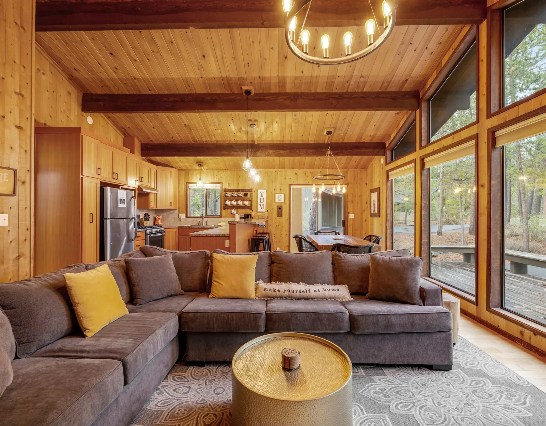 A living room with a sectional seating area, large windows, and an open kitchen.