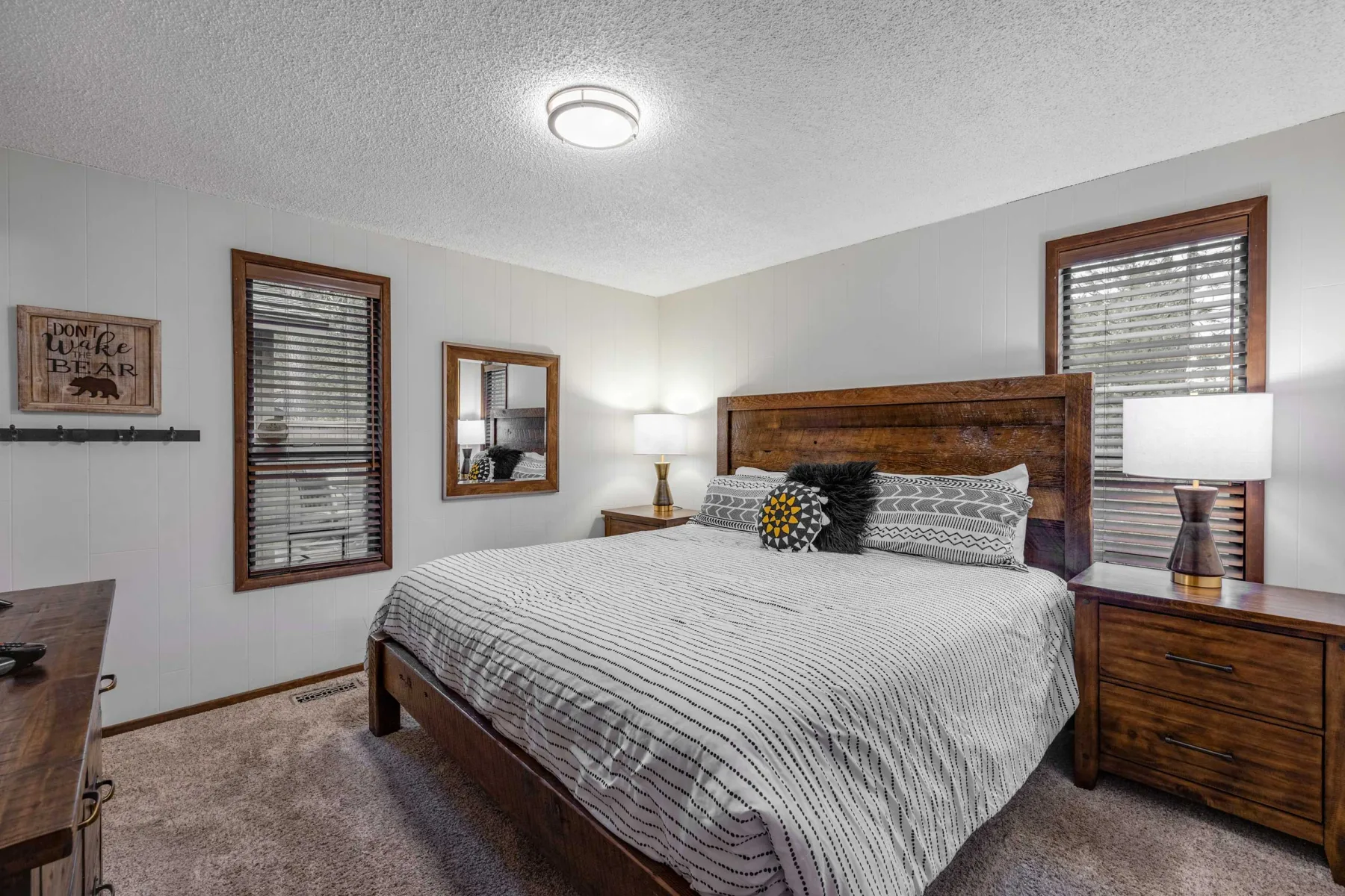 A bedroom with a large bed, bedside tables, and windows with blinds.