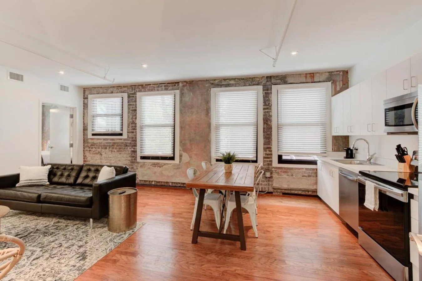Un espacio abierto de sala y cocina con una mesa de comedor junto a paredes de ladrillo visto.