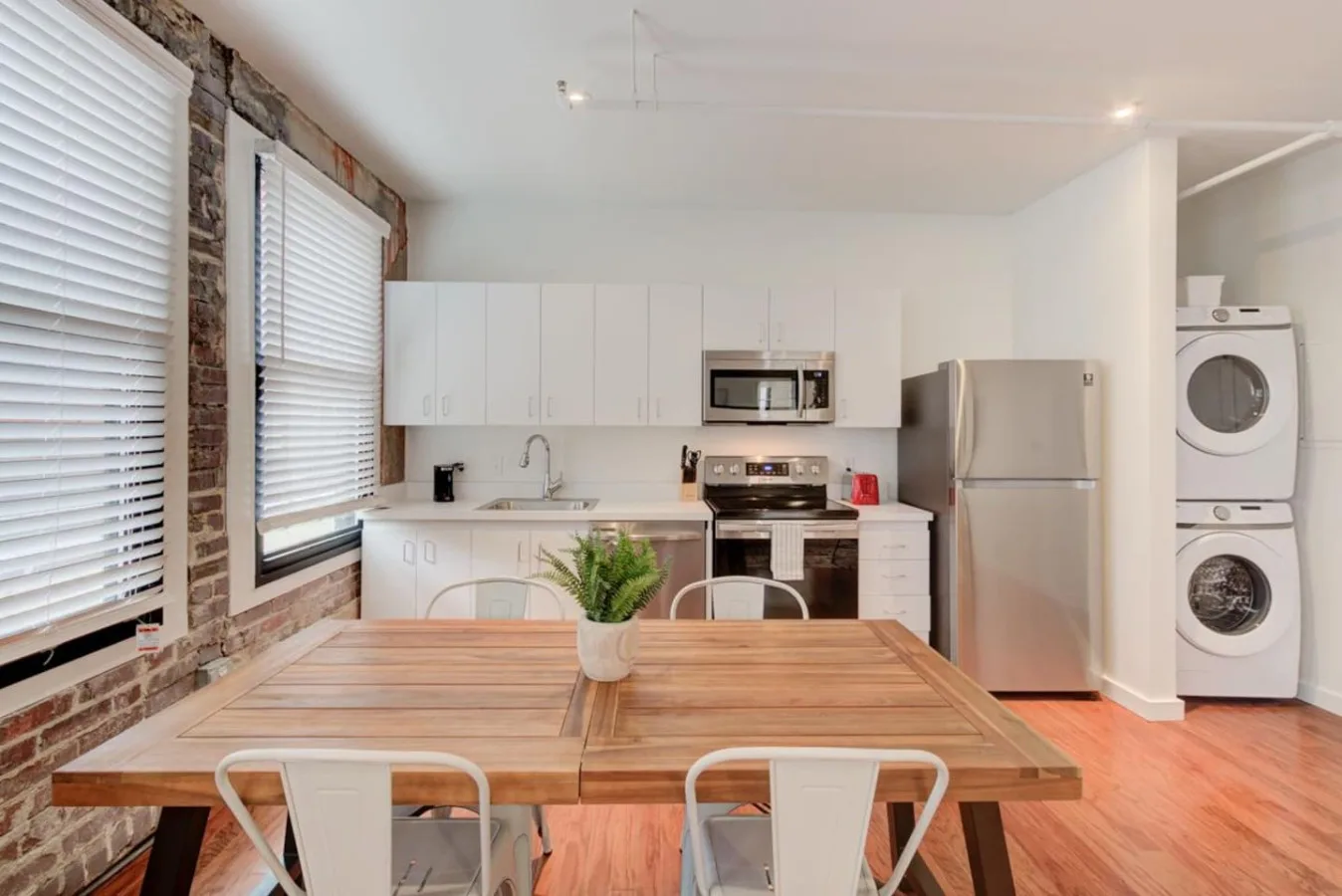 Una cocina y comedor luminosos con una mesa de madera y gabinetes blancos.