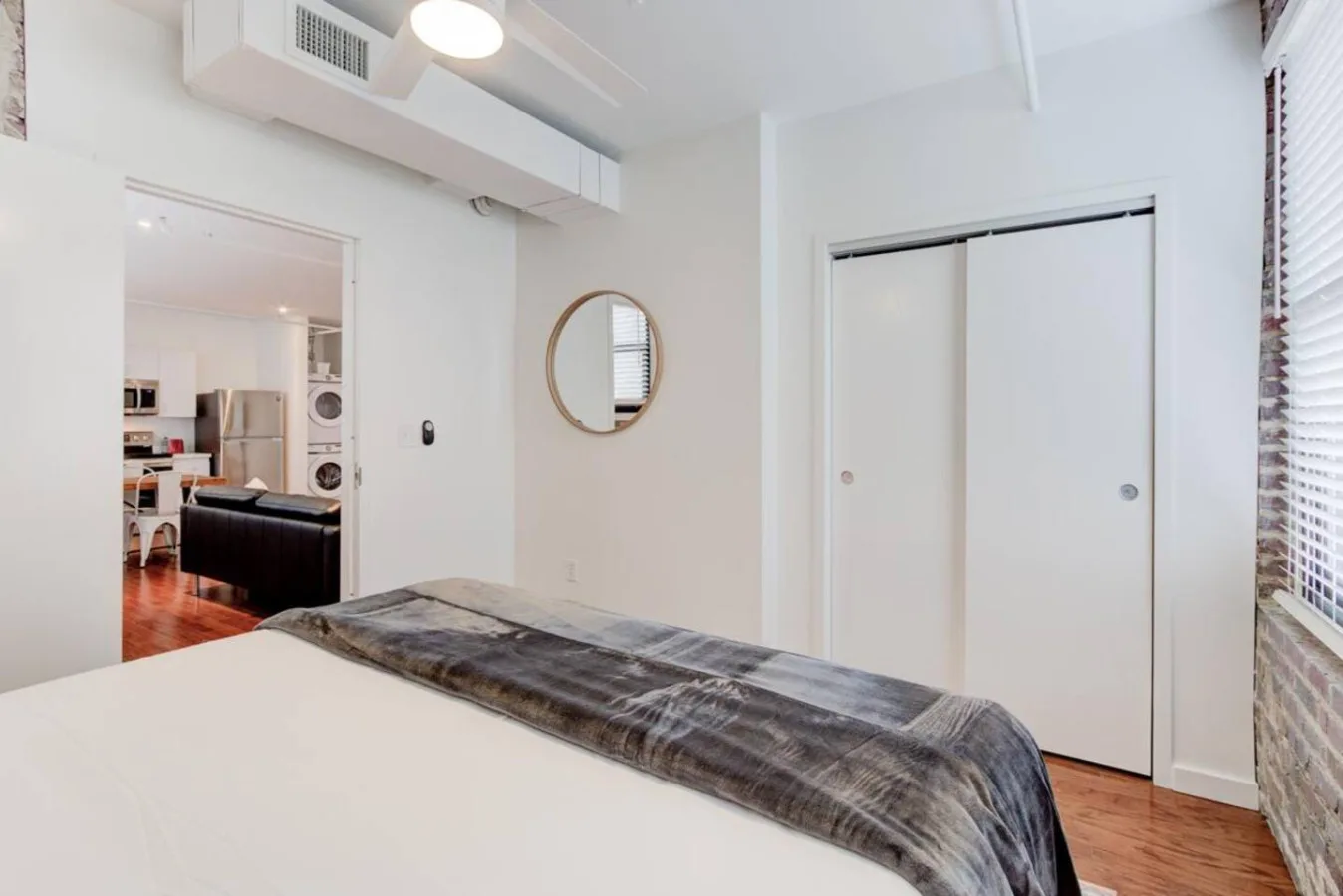 Un dormitorio luminoso con una cama, puertas corredizas de armario y un espejo redondo.