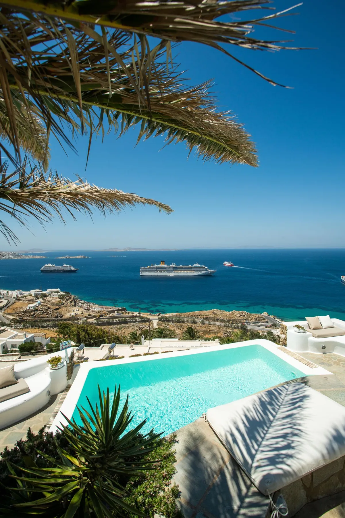 A turquoise pool overlooks the sea, with cruise ships visible offshore.