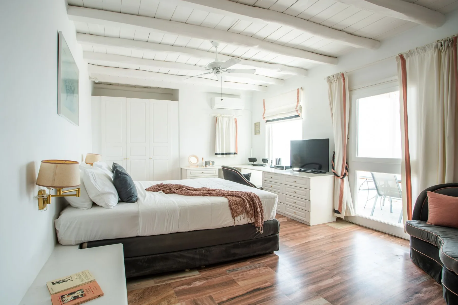 A bright bedroom with a bed, dresser, and large windows.