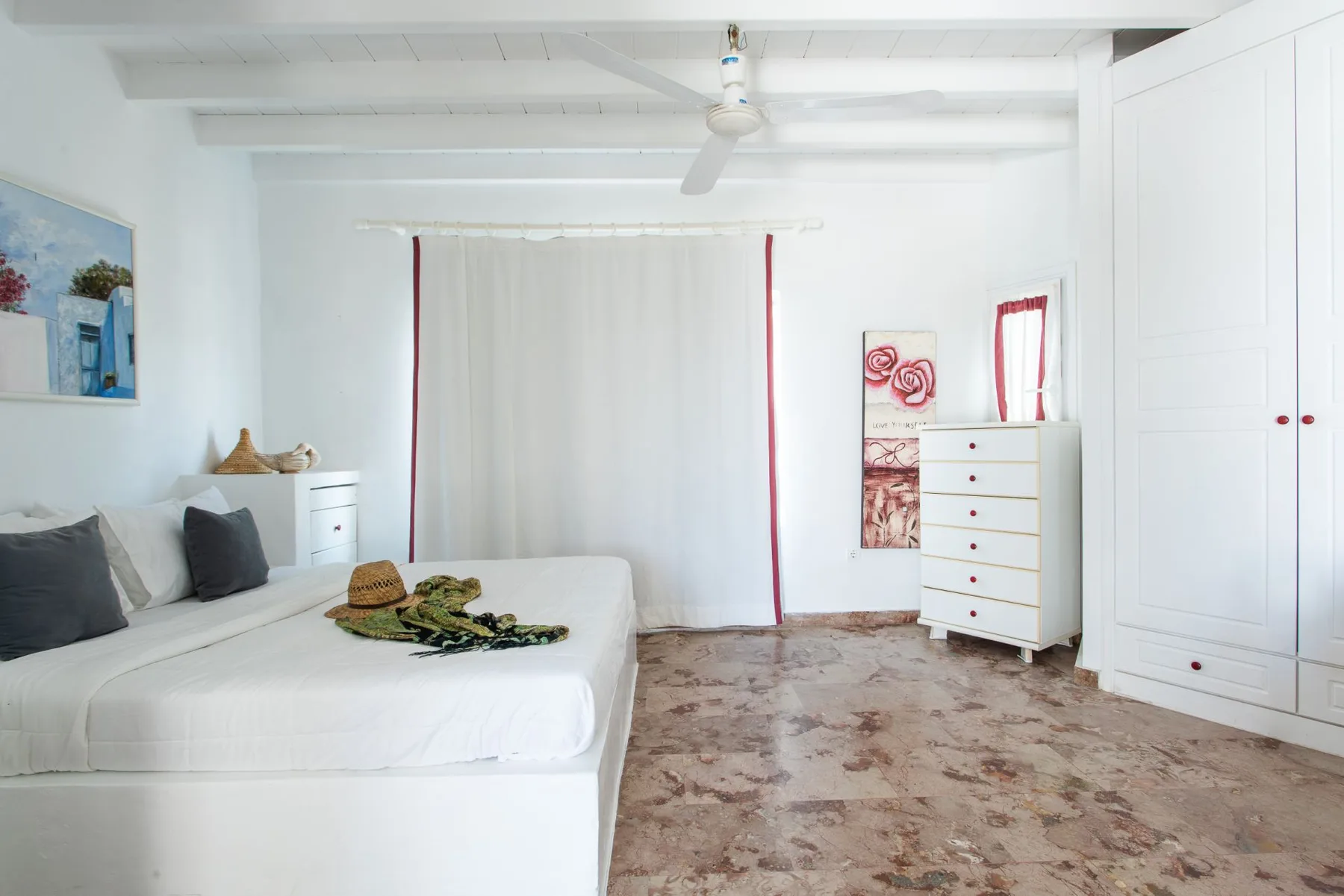 A bright bedroom with white bedding and a wide curtained window.
