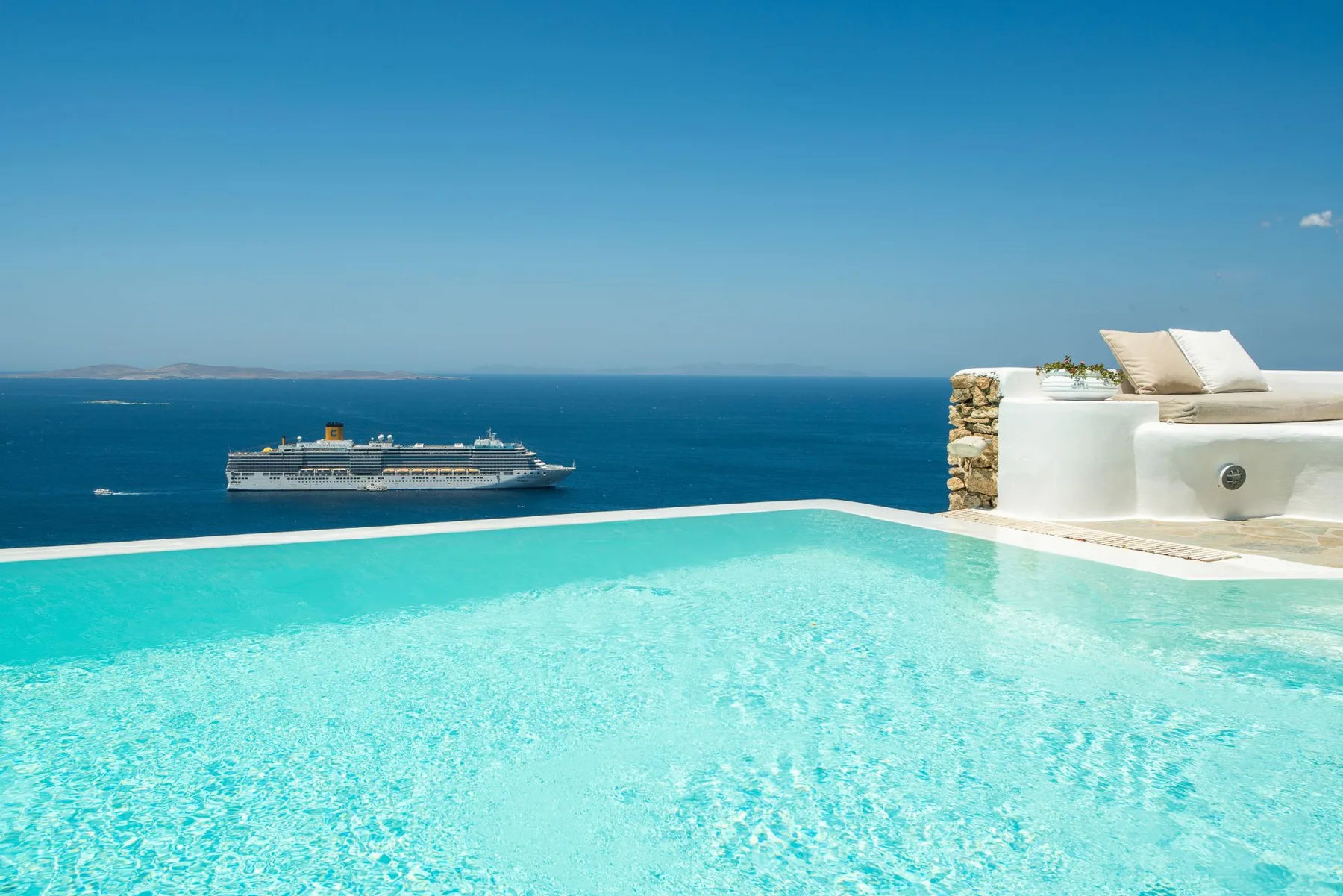 An outdoor swimming pool overlooks the sea, with a cruise ship on the horizon.