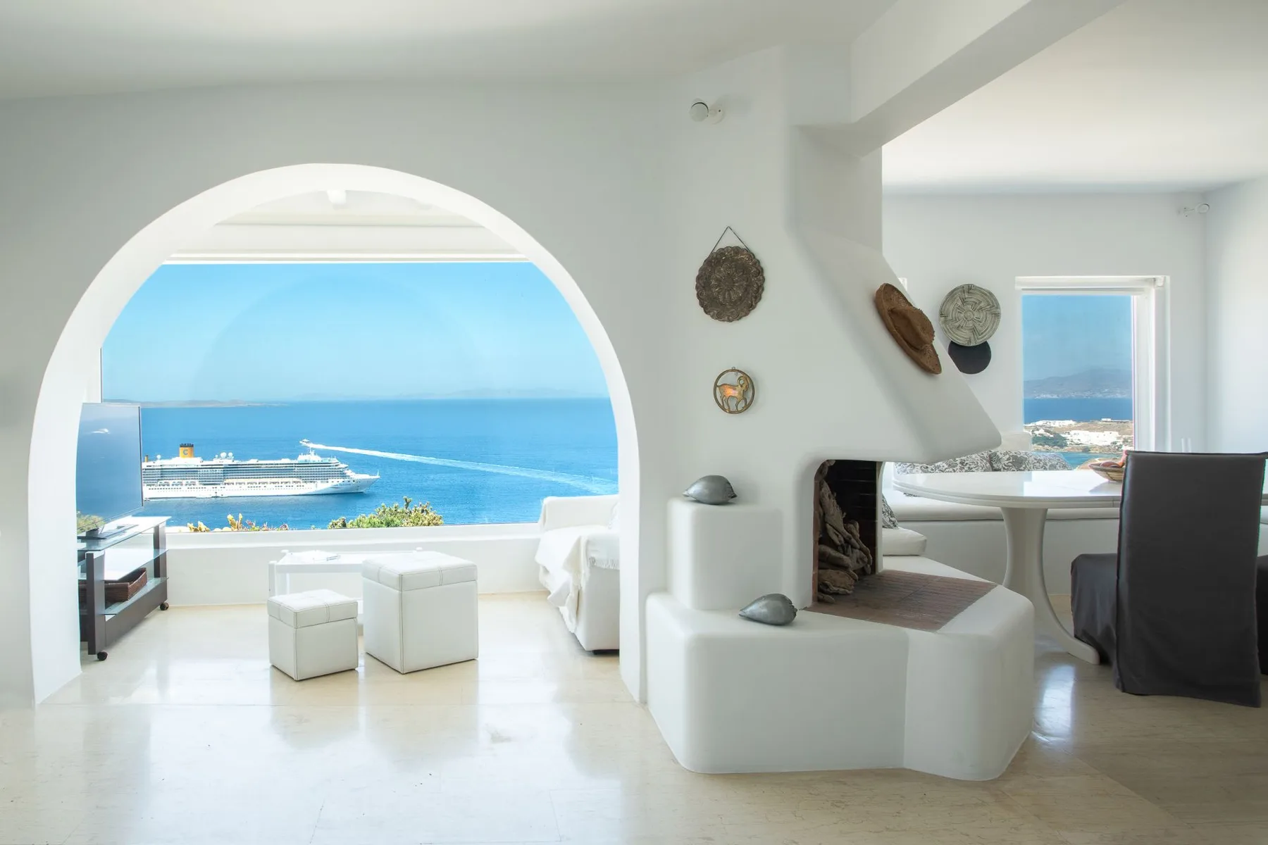 A bright living area opens onto a sea view, with white seating by a large arched opening.