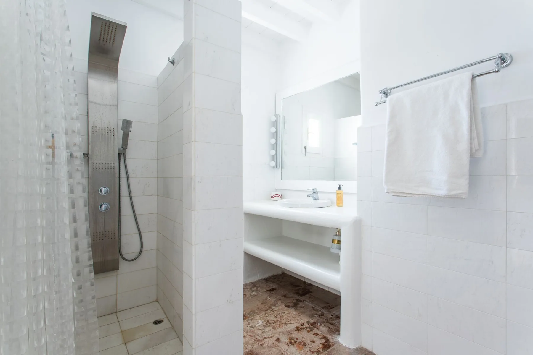 A bright tiled bathroom with a shower and a sink beneath a mirror.