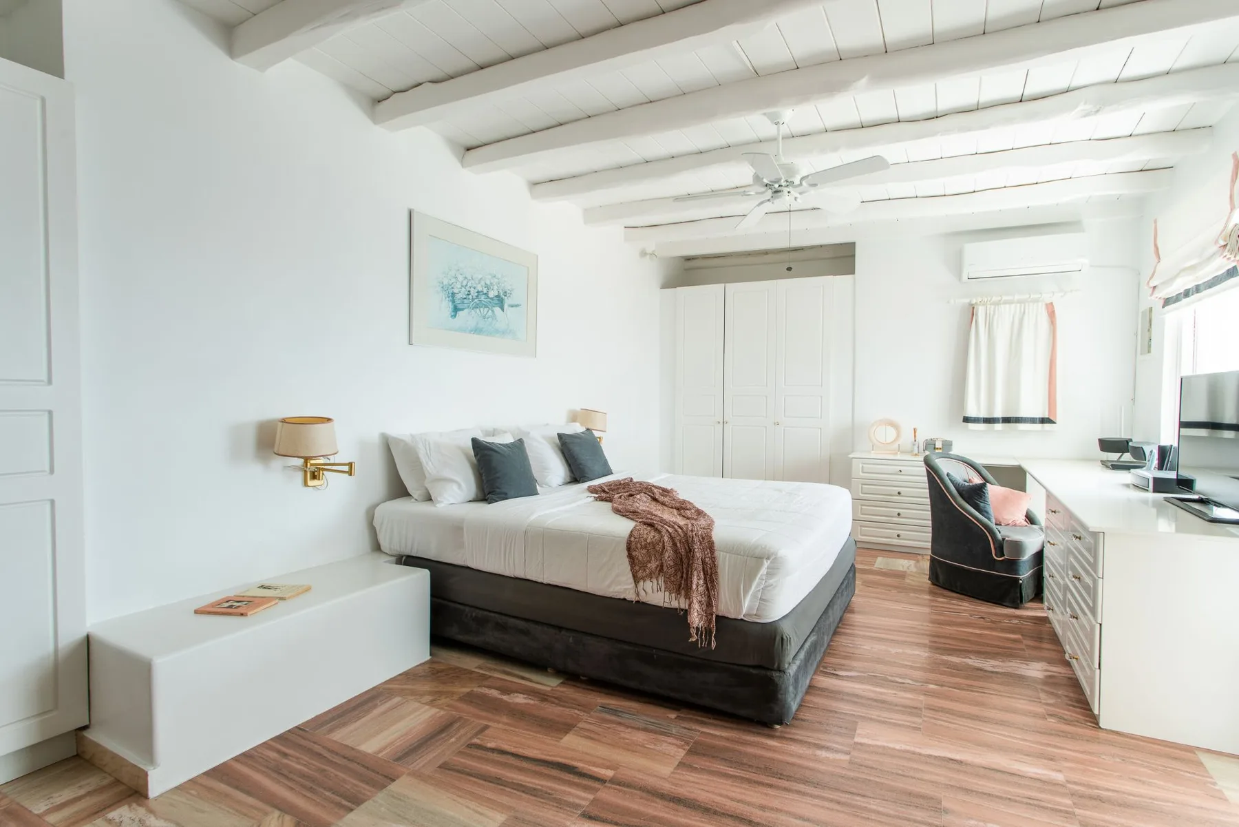 A bright bedroom with a bed, white walls, and wood flooring.