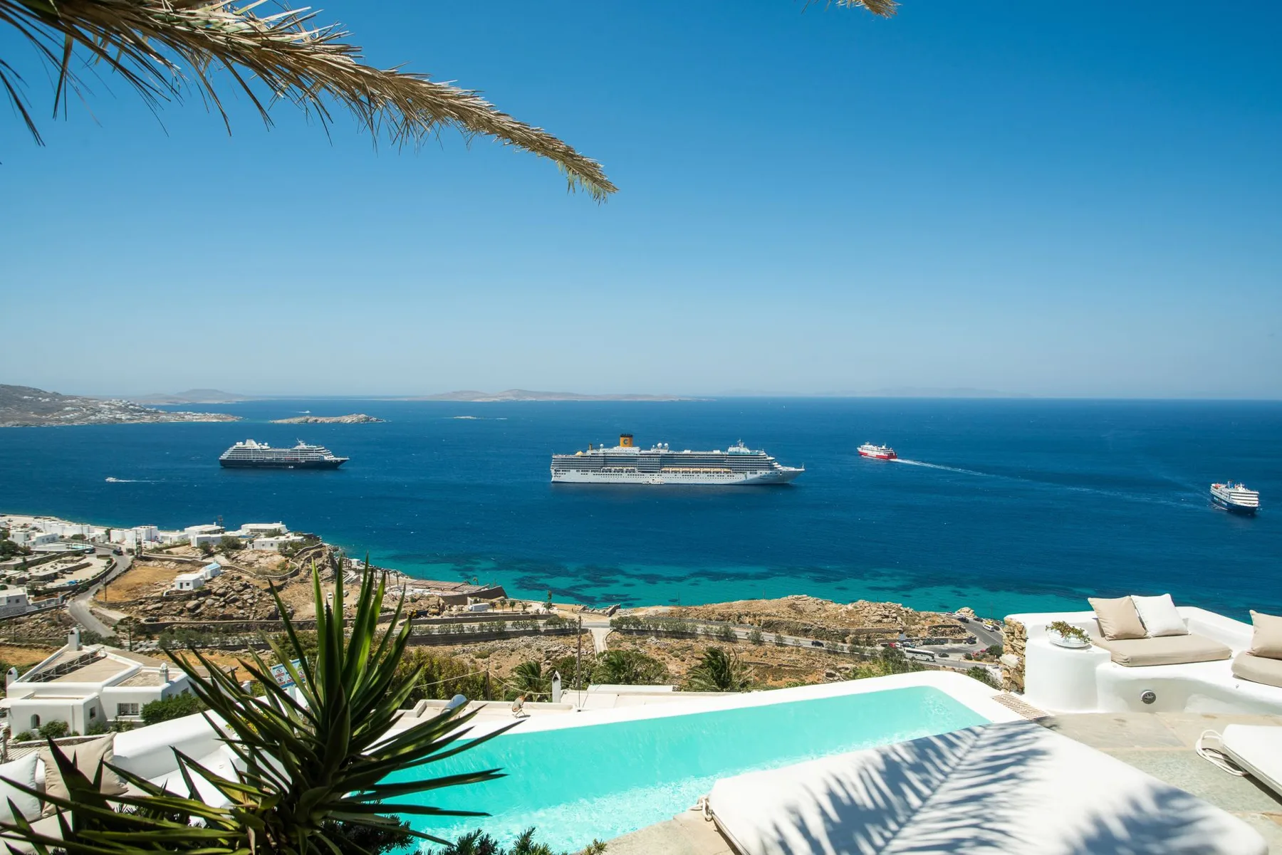 A turquoise pool overlooks a coastal bay with cruise ships on the water.