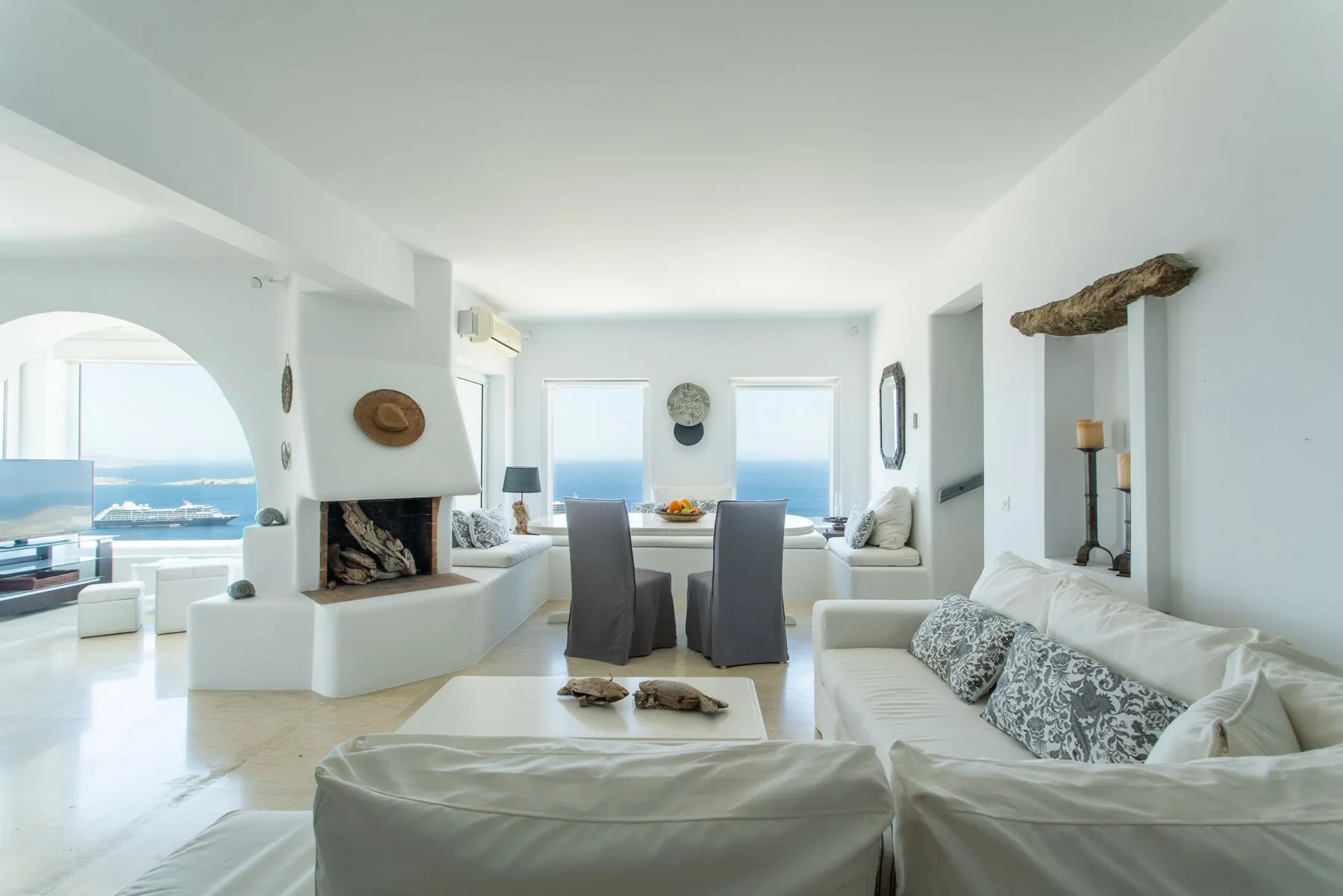 A bright living and dining area with white seating and a table by the windows.