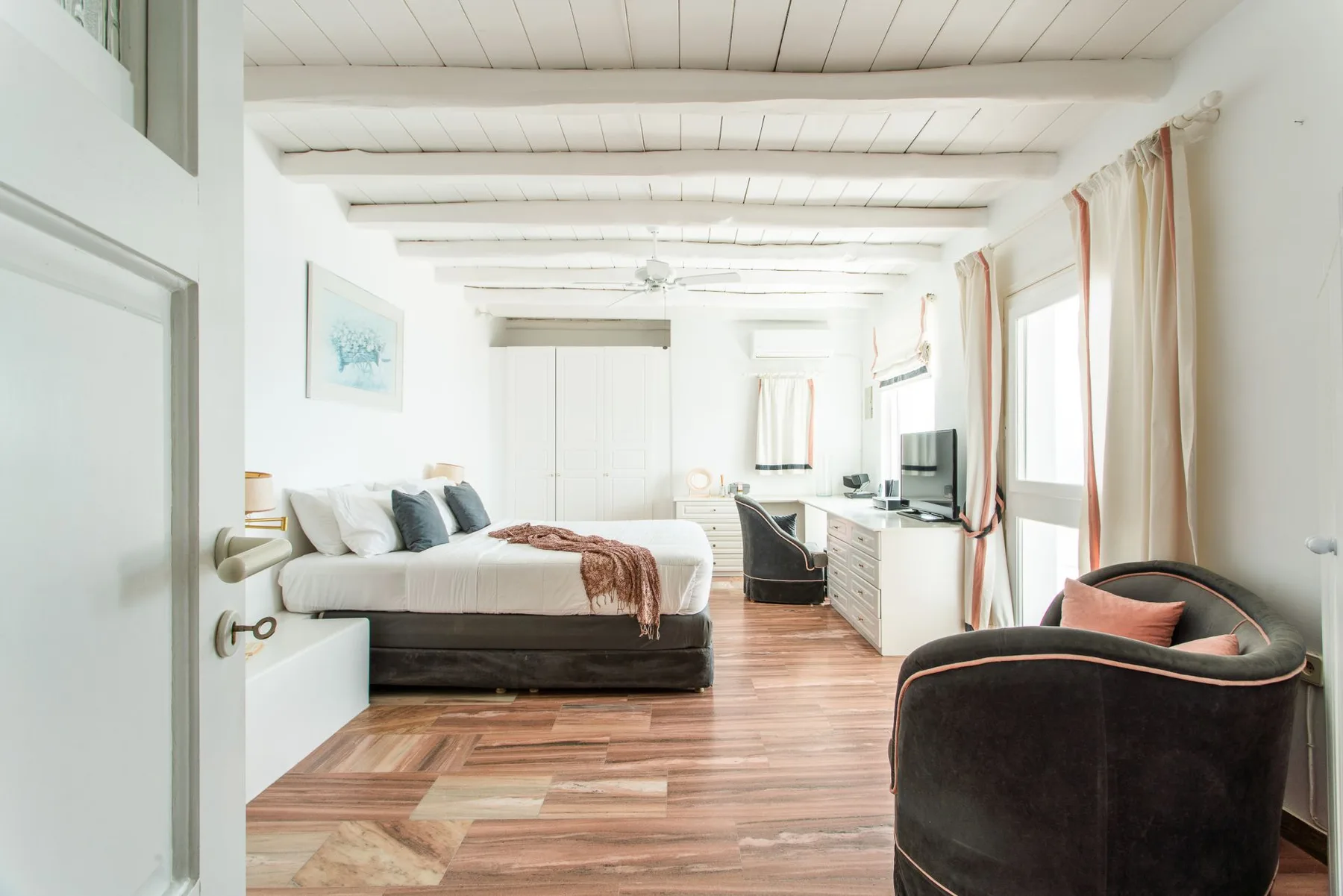A bright bedroom with a bed, a desk, and a dark upholstered chair.