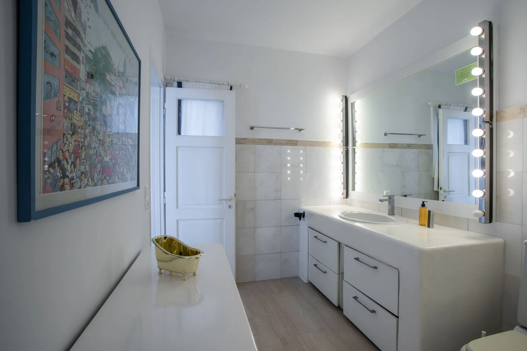 A bright bathroom with a long vanity, wide mirror, and tiled walls.