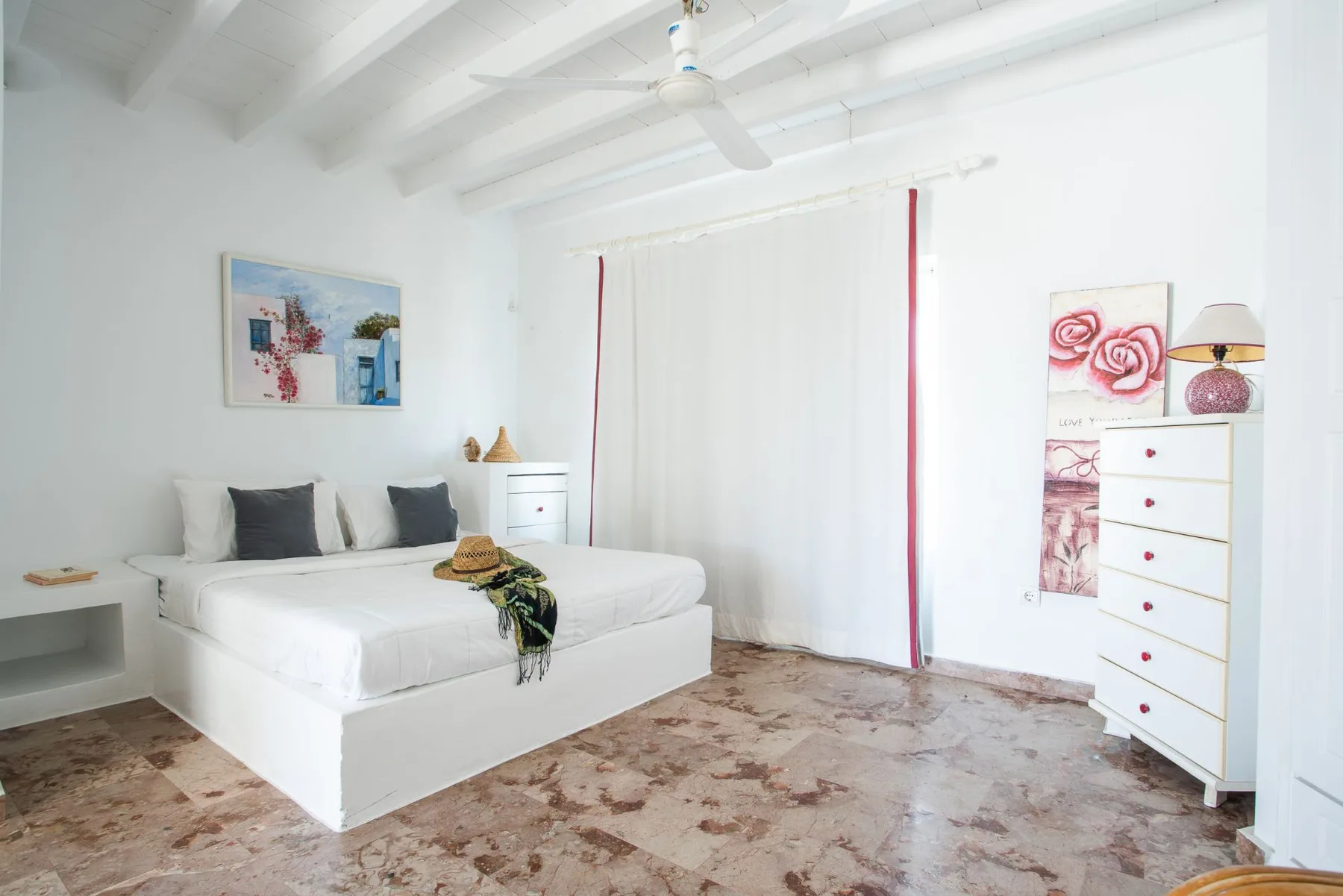 A bright bedroom with a white bed and floor-length curtains.