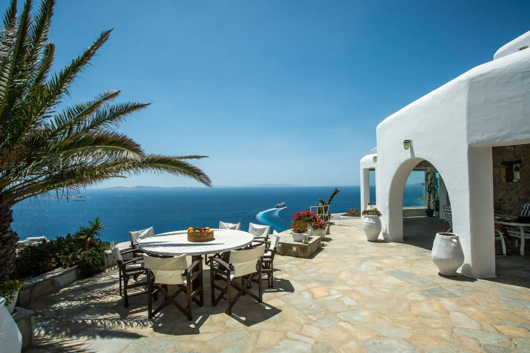 A seaside terrace with a dining table and seating overlooking the blue water.