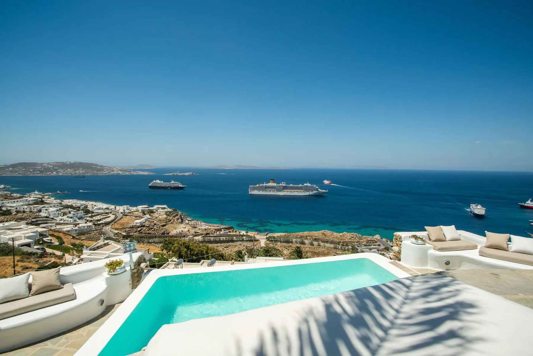 A rooftop pool overlooks the coastline and several boats on the sea.