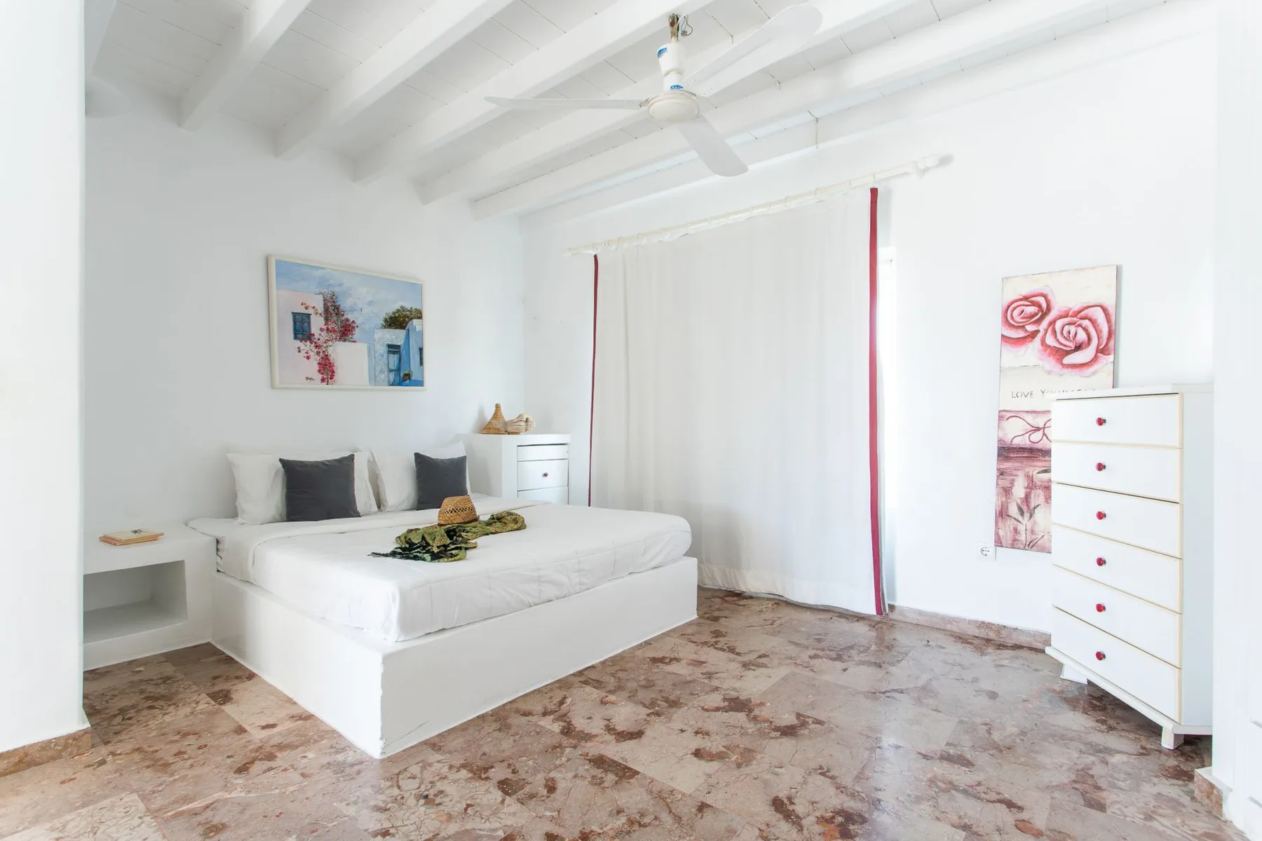 A bright bedroom with a white bed beneath exposed ceiling beams.